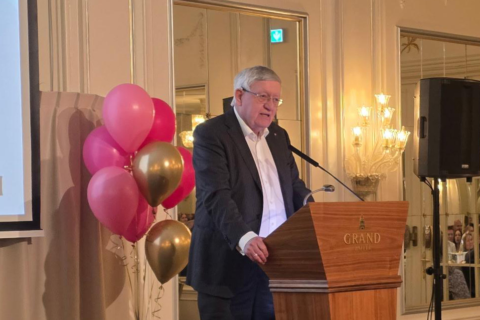 En person som står ved en talerstol med ballonger bak seg