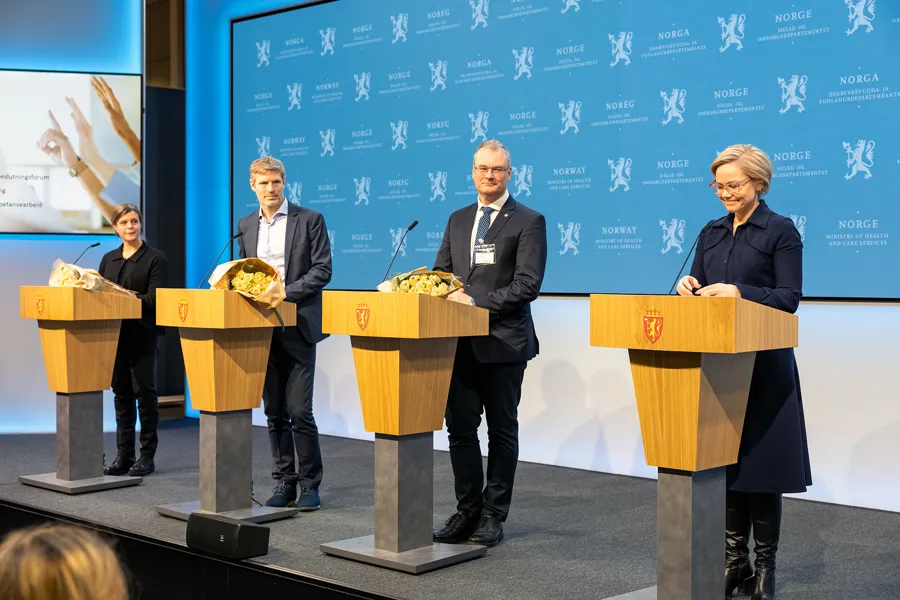 En gruppe mennesker som står på talerstoler med en person stående bak seg