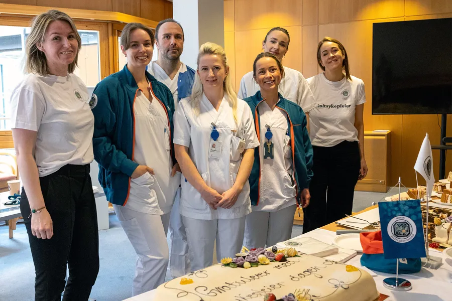 En gruppe mennesker i hvite labfrakker som står ved siden av en kake