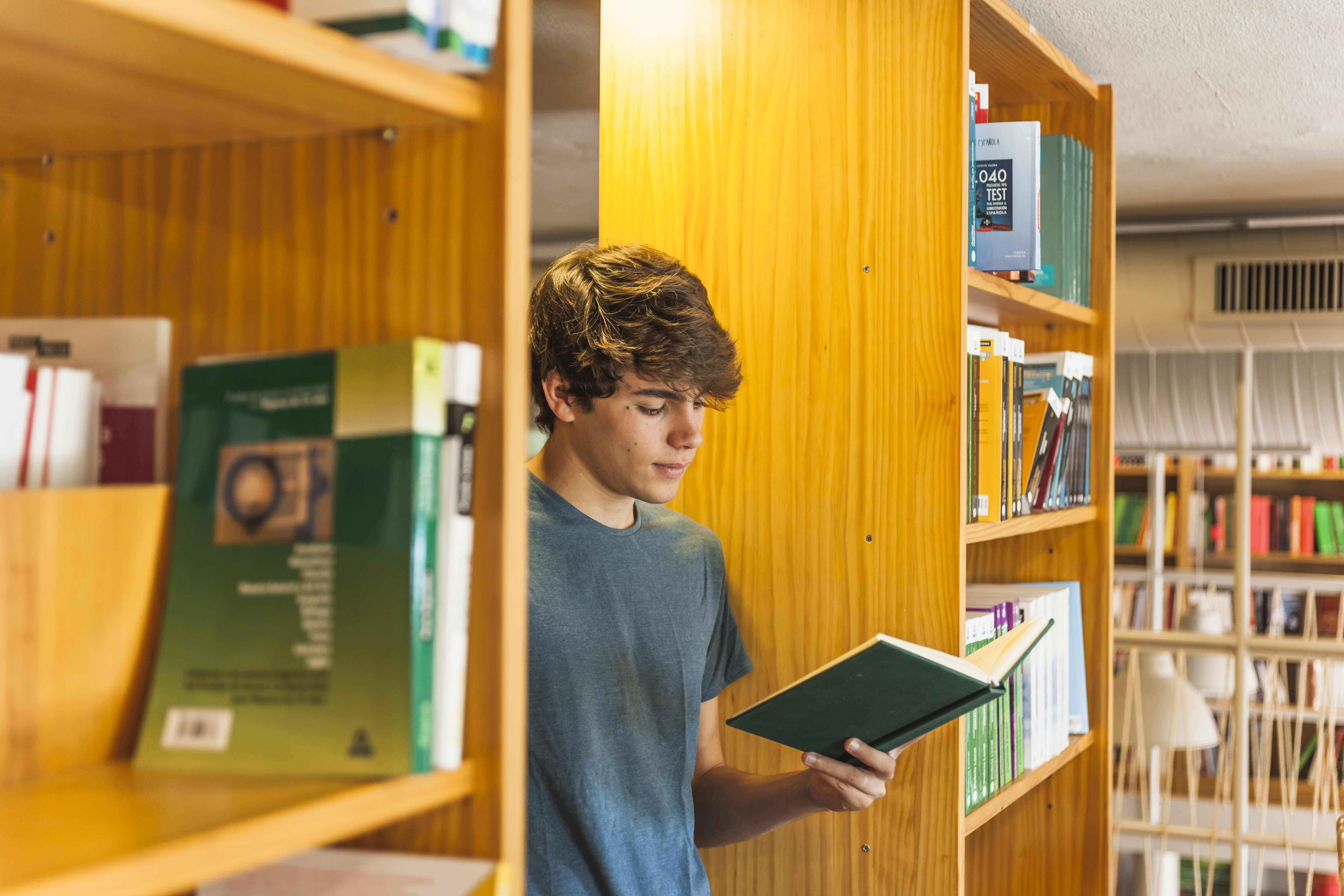 Ung mann står inntil en hylle og leser i en bok