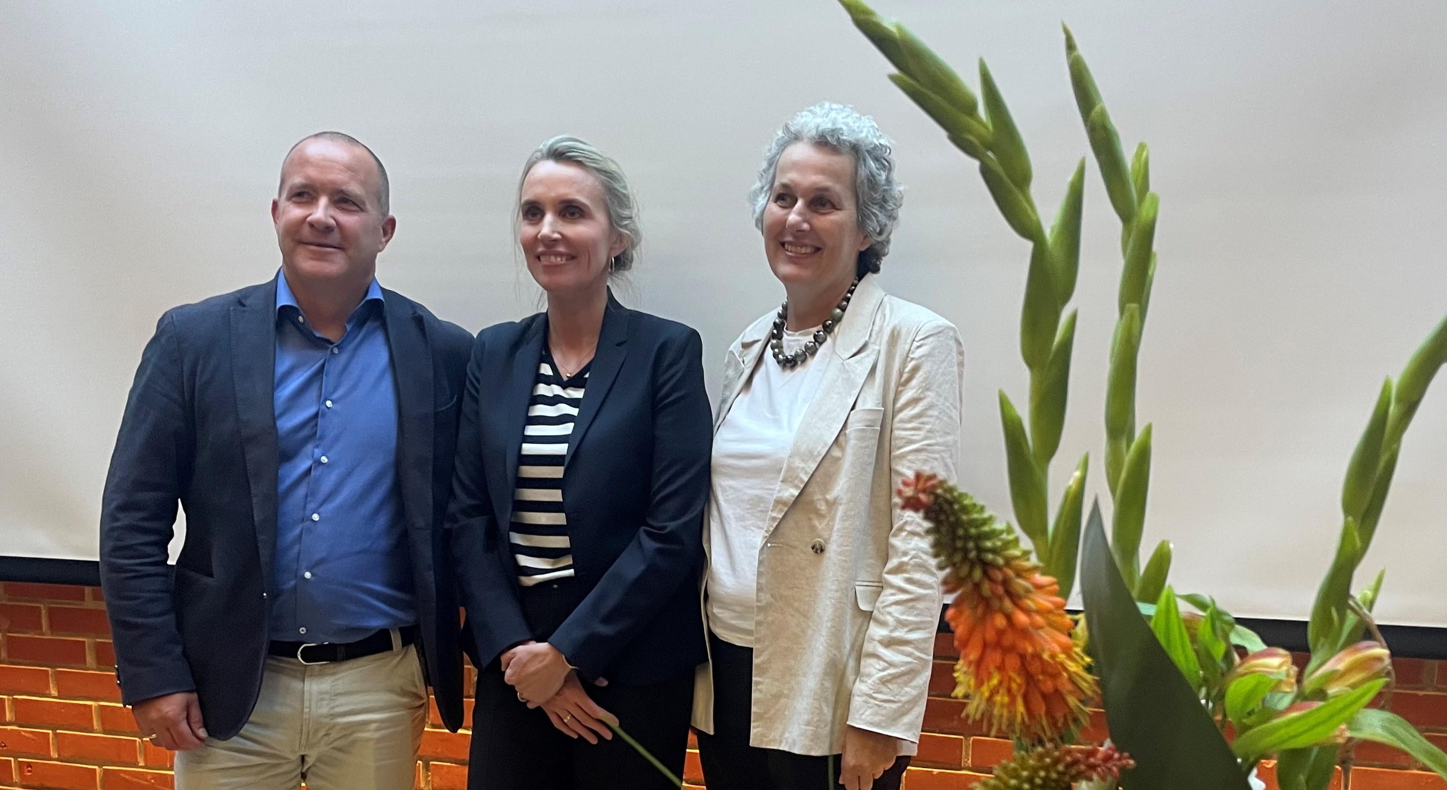 Tre smilende personer. En mann og to damer. 