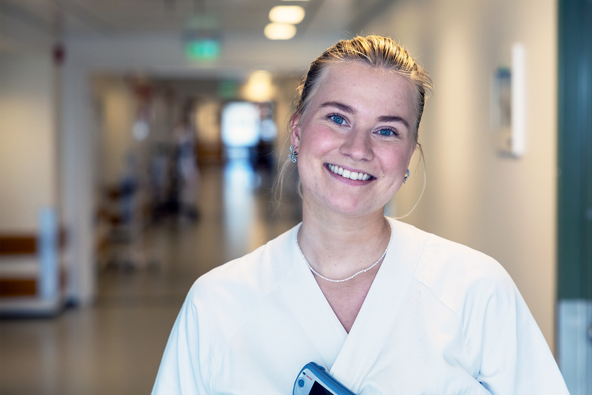 Sykepleier i uniform som står i en sykehuskorridor.