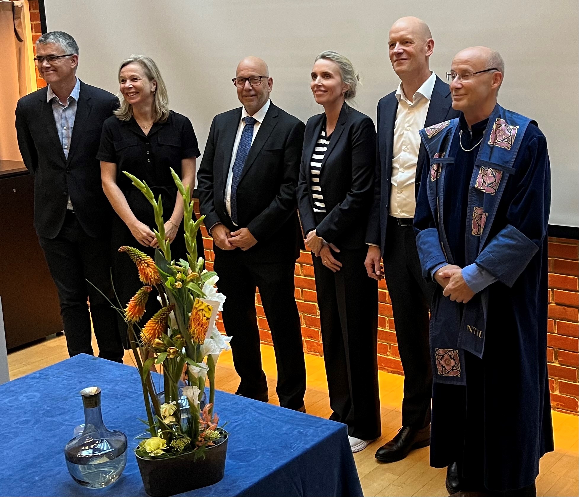 Seks smilende mennesker blir gratulert. To kvinner og fire menn. De er pent kledd.