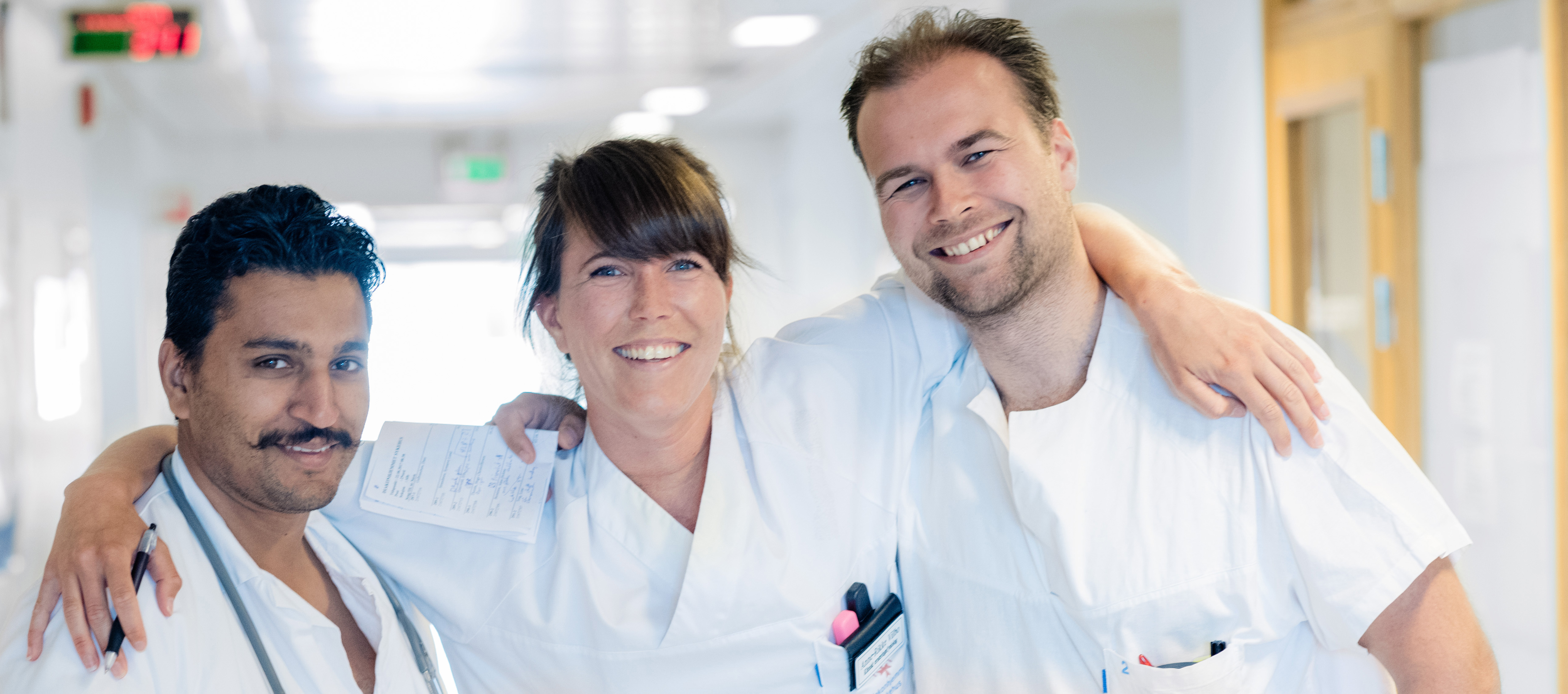 Tre leger holder rundt hverandre og smiler til kamera