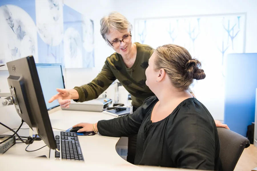 En kvinne som viser en mann noe på datamaskinen