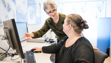 En kvinne som viser en mann noe på datamaskinen