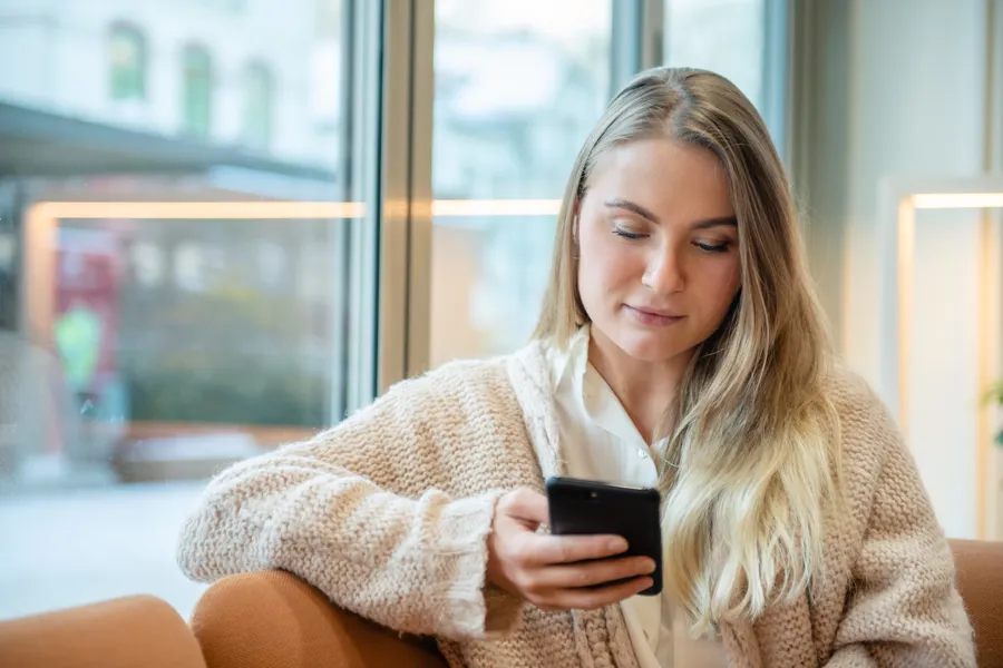 Kvinne som sitter og ser på en mobiltelefon
